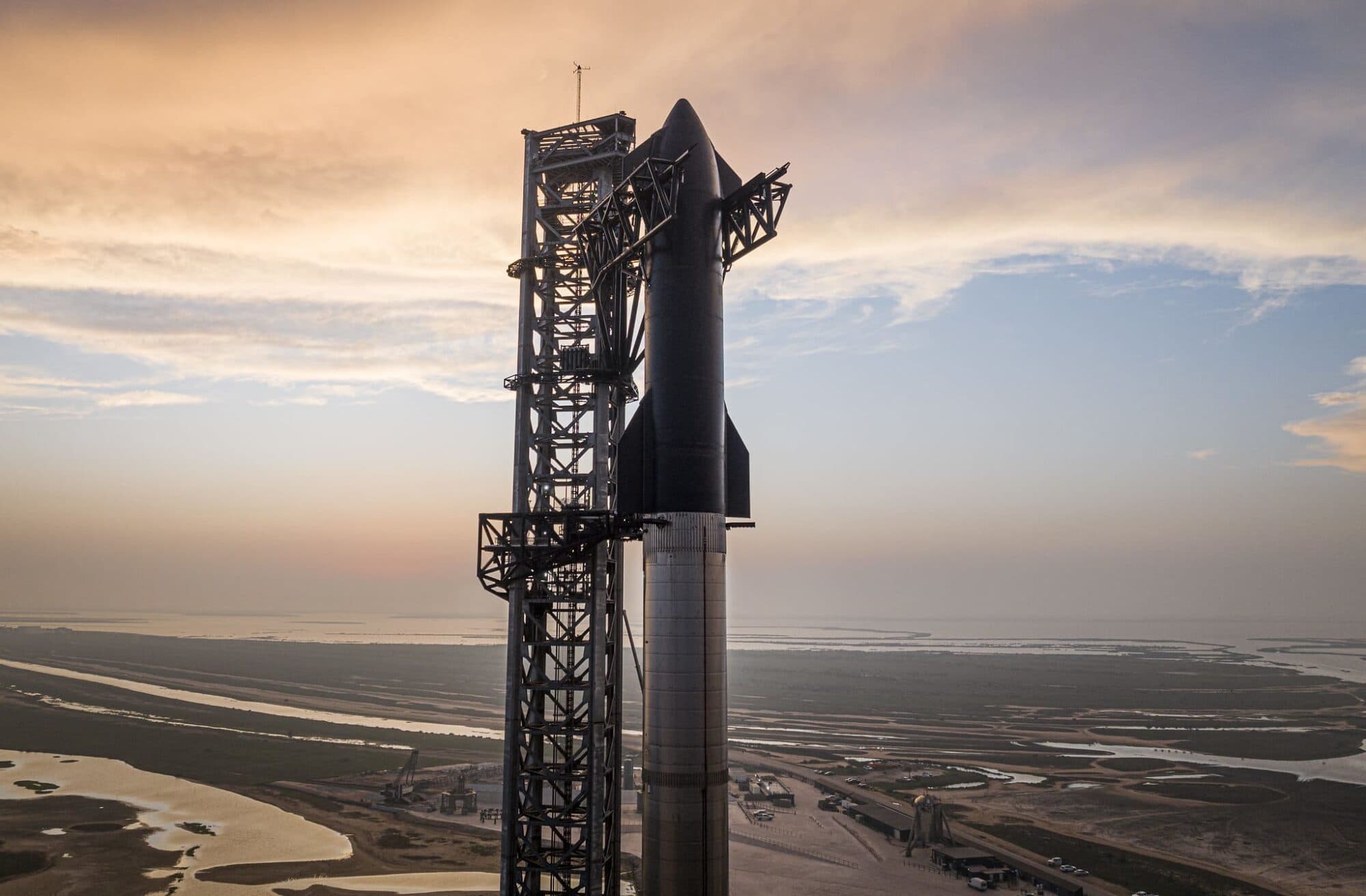The Starbase launch tower and a stacked Starship at sunset.